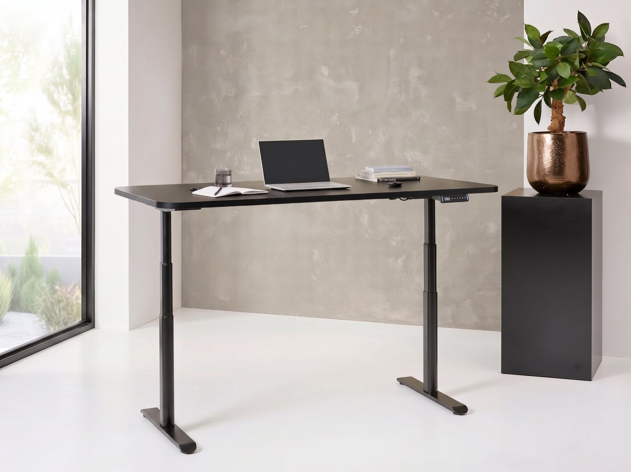 Black adjustable desk in a modern office setting with a laptop and plant.