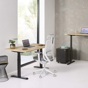 Modern office setup with adjustable desks and a chair in a bright room.