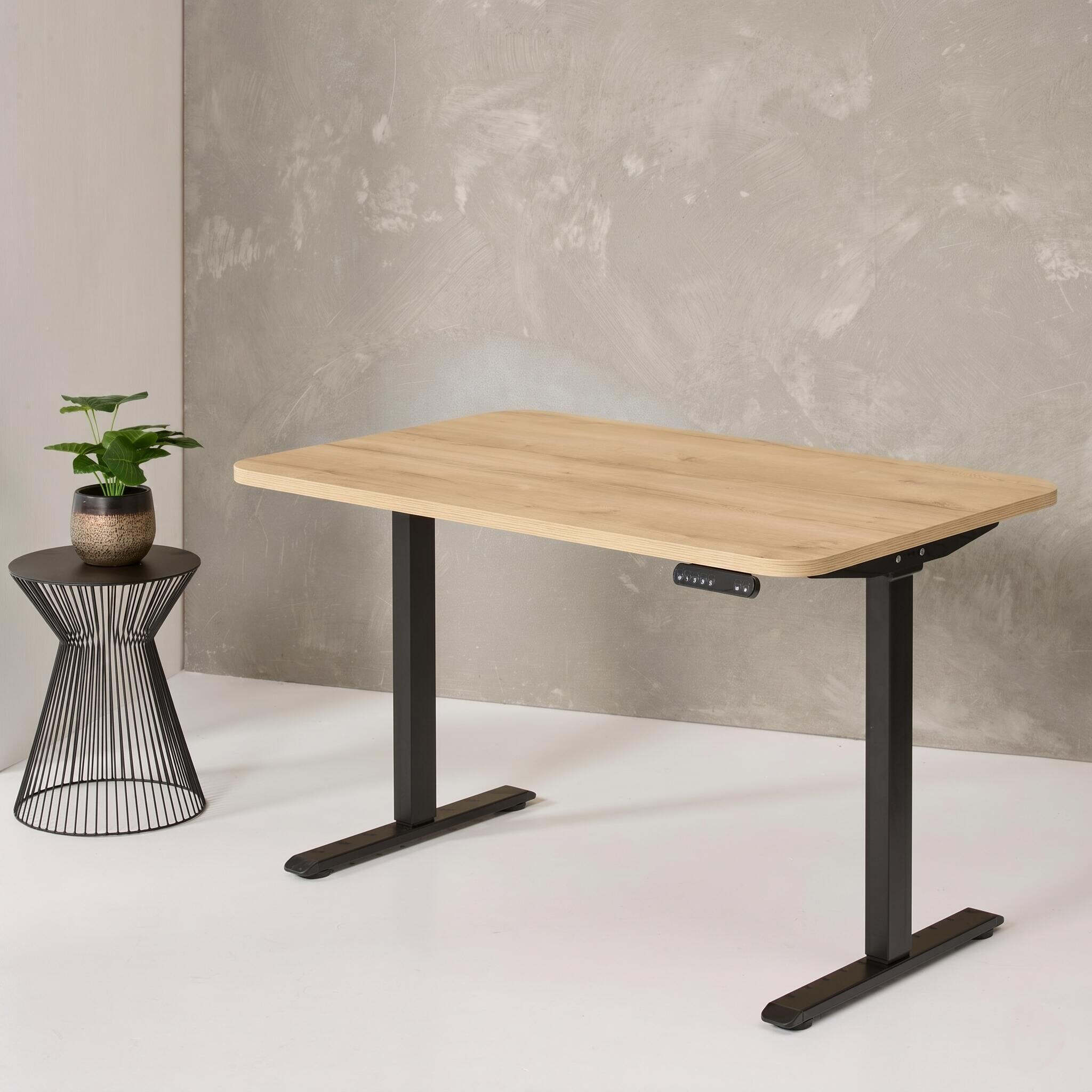 Wooden stand-up desk with black legs next to a small plant on a wire side table against a concrete wall.