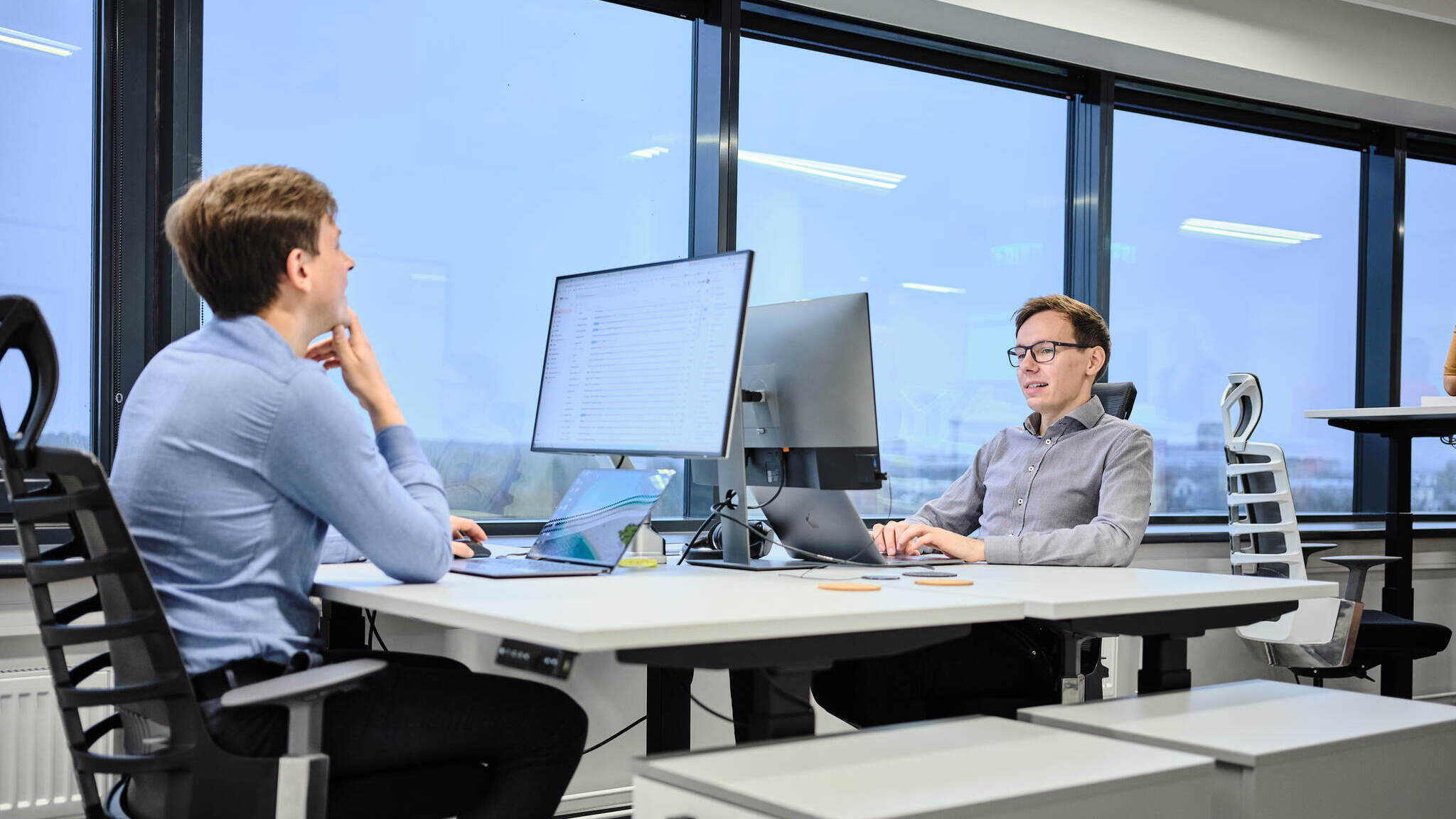 Two people sitting at a desk with computers in an office setting
